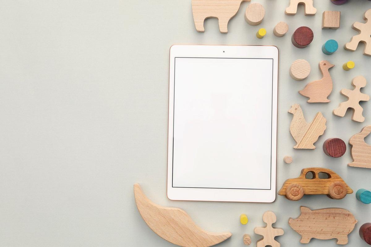 Tablet leżący ekranem w dół na półce obok drewnianych zabawek i książek dla dzieci