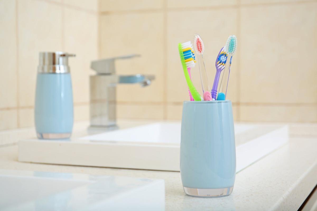 Dwie szczoteczki w ceramicznych kubeczkach na umywalce obok klepsydry