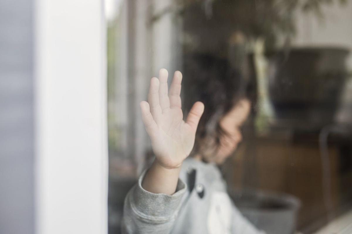 Mała dłoń dziecka machająca przez okno przedszkola, widziana z zewnątrz
