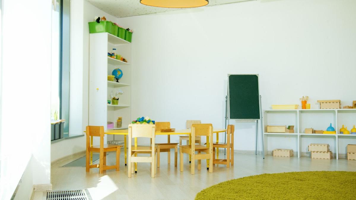 Kolorowa sala przedszkolna z małymi stolikami i krzesełkami, zabawki na półkach